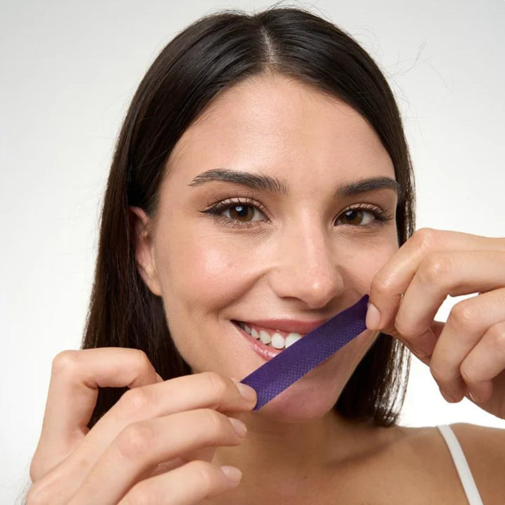 Woman holding a purple whitening strip close to her face against a white background